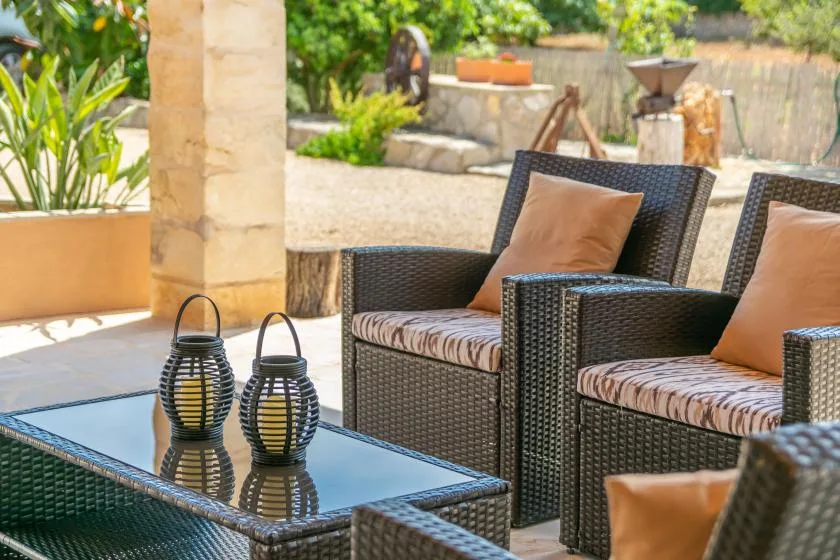 Asientos en un patio al aire libre con sillas tejidas y una mesa de vidrio.