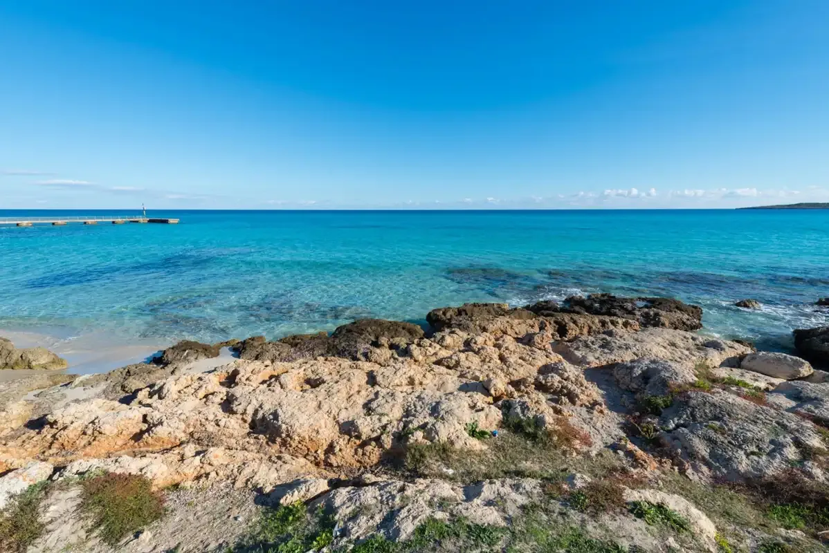 Una costa rocosa bordea aguas turquesas y claras bajo un cielo azul.