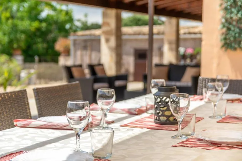 Un comedor exterior a la sombra, con una mesa puesta con cristalería y platos.