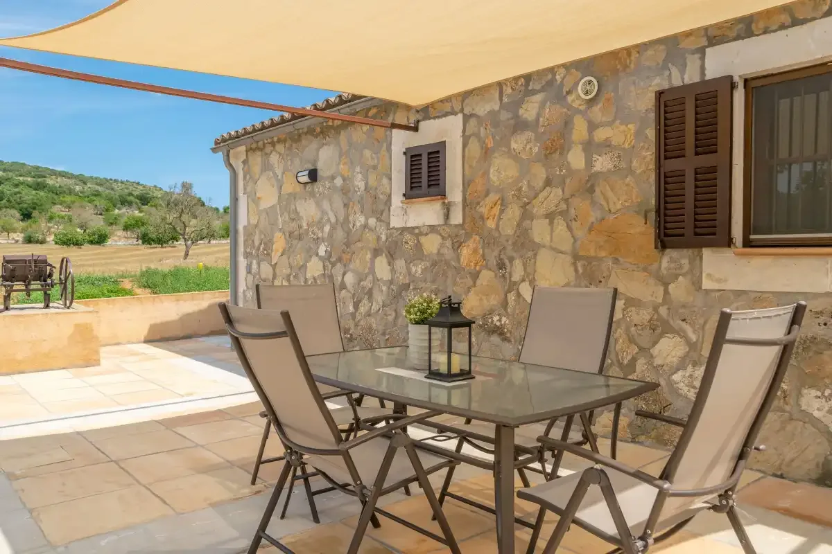 Un patio de piedra con una mesa de vidrio y asientos al aire libre bajo un toldo.