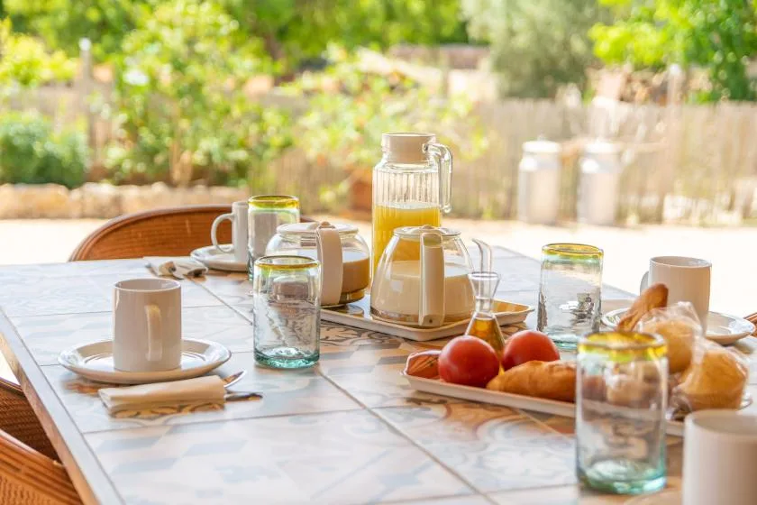 Una mesa de comedor al aire libre está preparada con bebidas, fruta y pan.