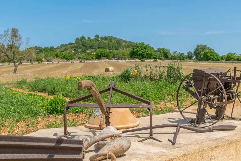 Un campo rural con equipo agrícola antiguo en primer plano y colinas verdes al fondo.