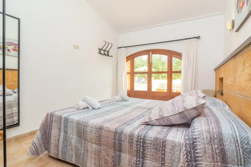 Un dormitorio con una colcha estampada y una ventana arqueada de madera.