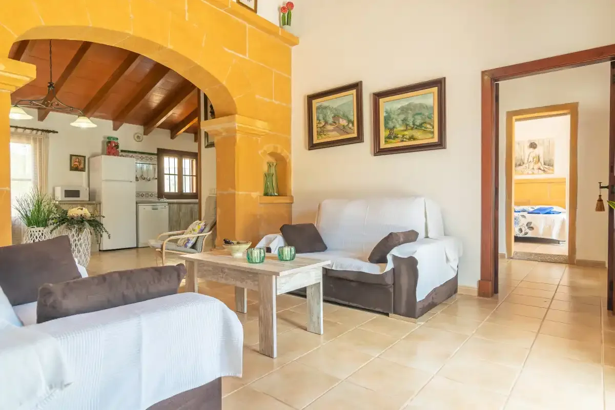 Sala de estar con asientos y una cocina con vigas de madera al otro lado de un arco.