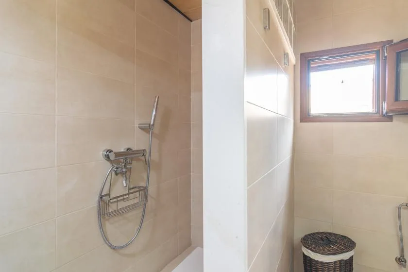 Un baño con azulejos, una ducha de pared y una ventana pequeña.