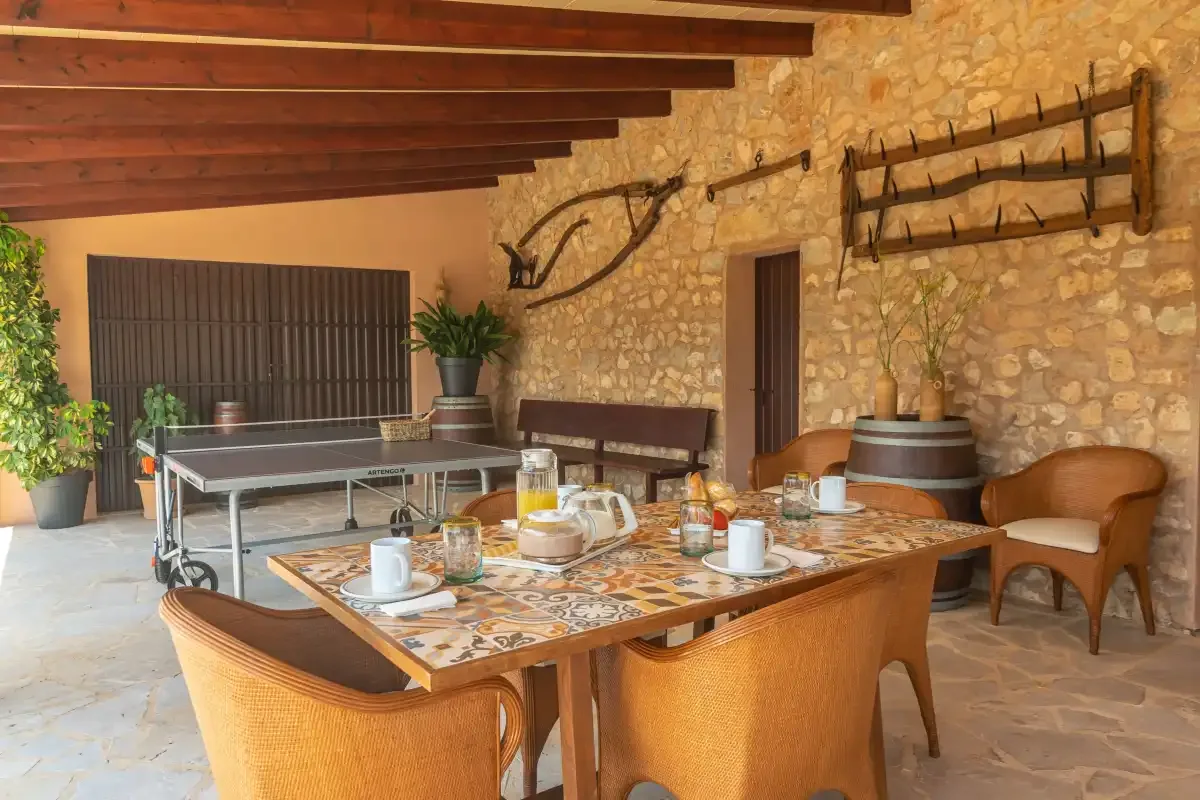 Comedor rústico con una mesa preparada junto a una pared de piedra y una mesa de ping-pong.