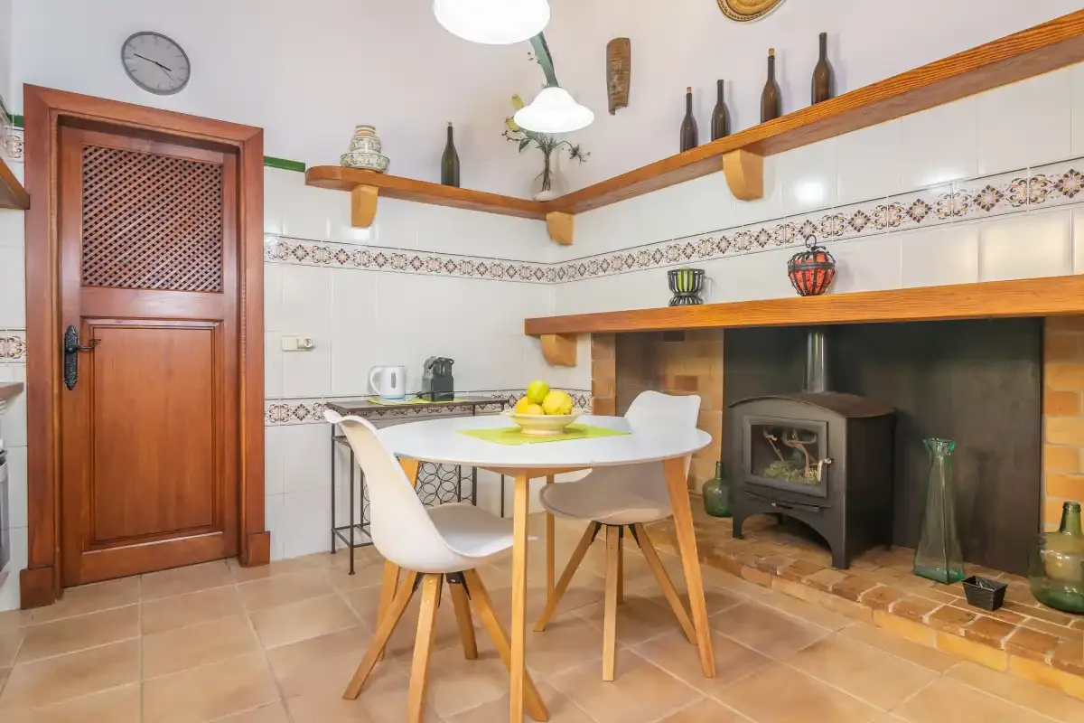 Comedor con suelo de baldosas y una mesa junto a una estufa de leña.