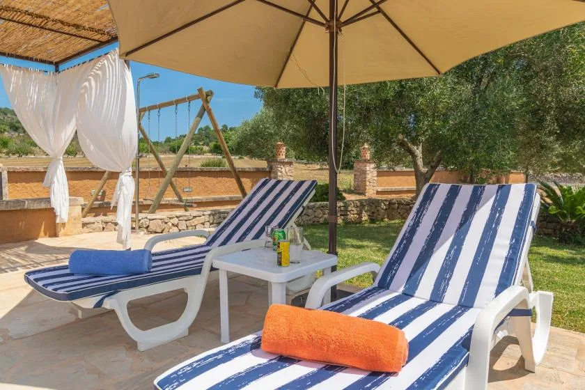 Un patio soleado con asientos reclinables a rayas bajo una sombrilla grande.