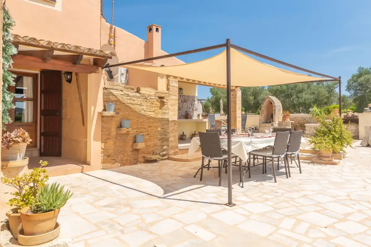 Un patio soleado de piedra tiene una mesa de comedor a la sombra y asientos.