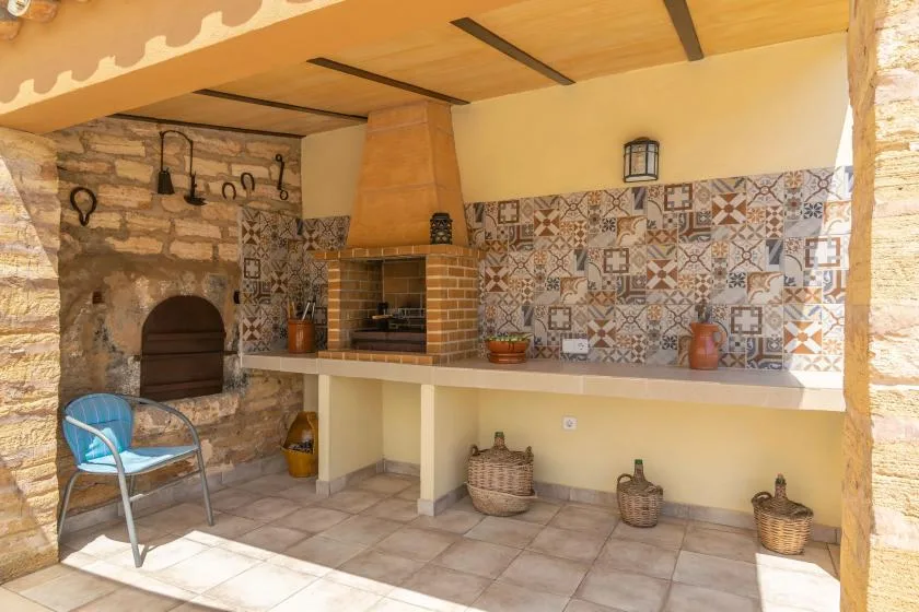 Una cocina exterior cubierta con parrilla de ladrillo, pared de azulejos y asientos.
