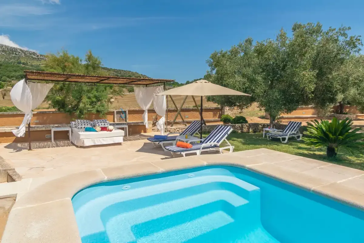 Una piscina al aire libre con tumbonas y una zona de descanso a la sombra.