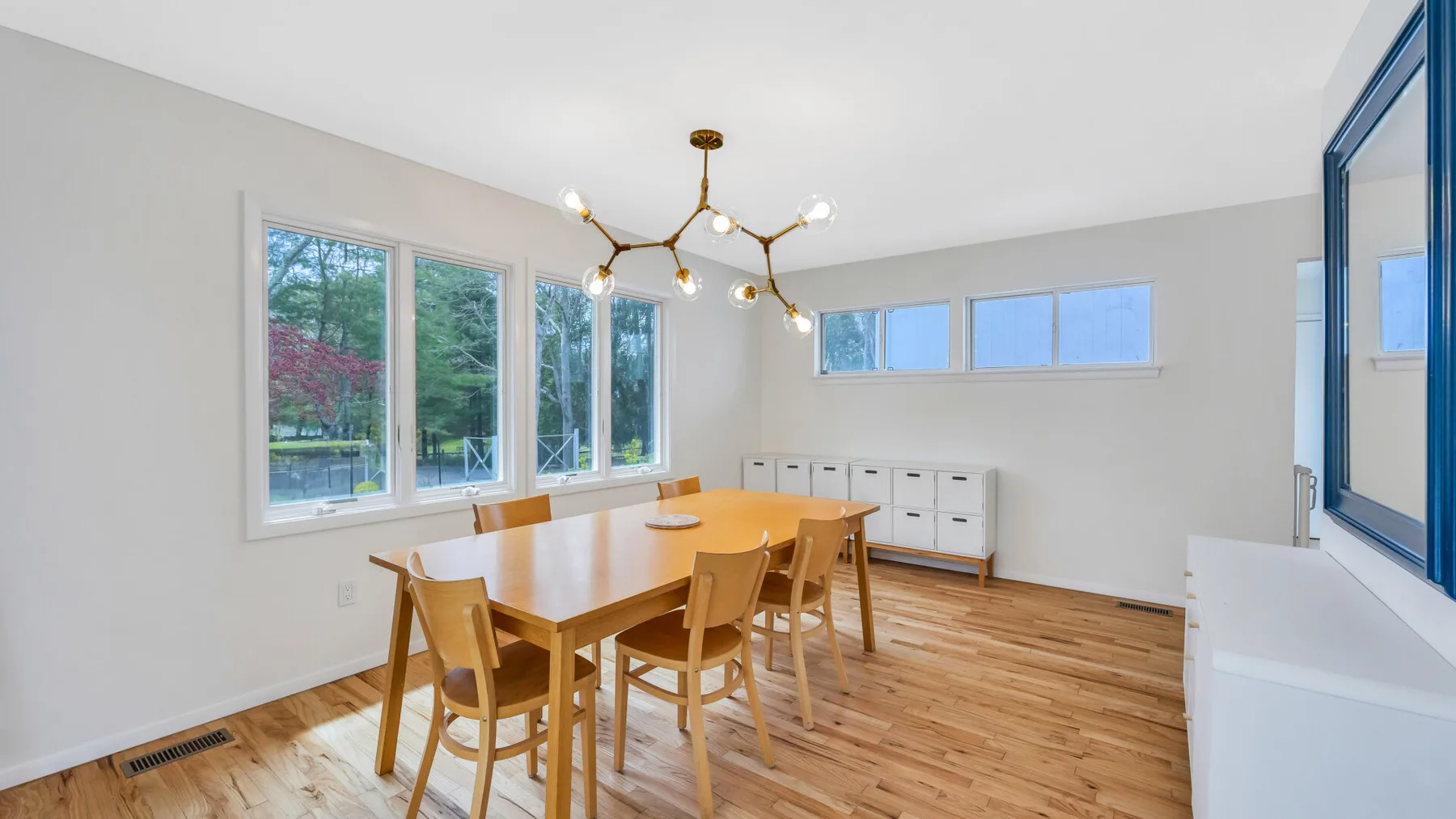 A bright dining area has a wooden table and chairs beside large windows.
