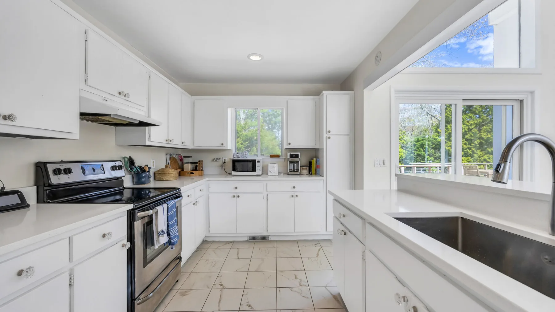 A bright kitchen with white cabinets, an oven, and a large sink.
