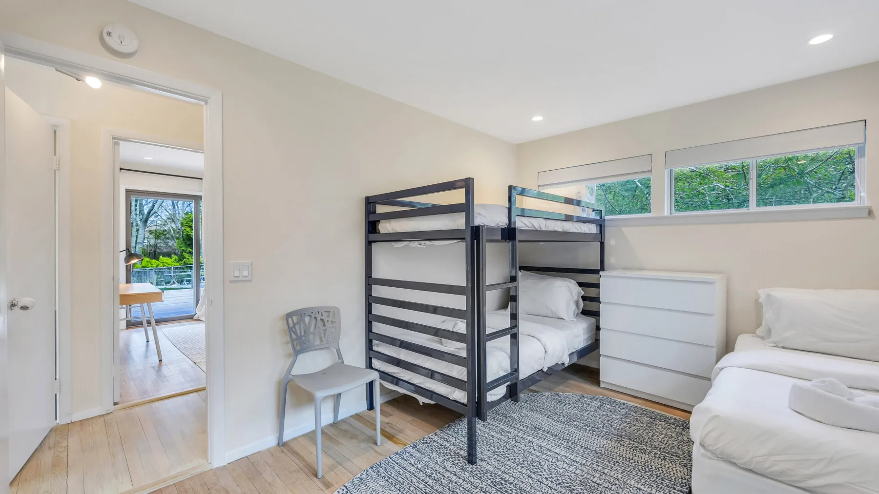 A bedroom with bunk beds, a dresser, and a window overlooking greenery.