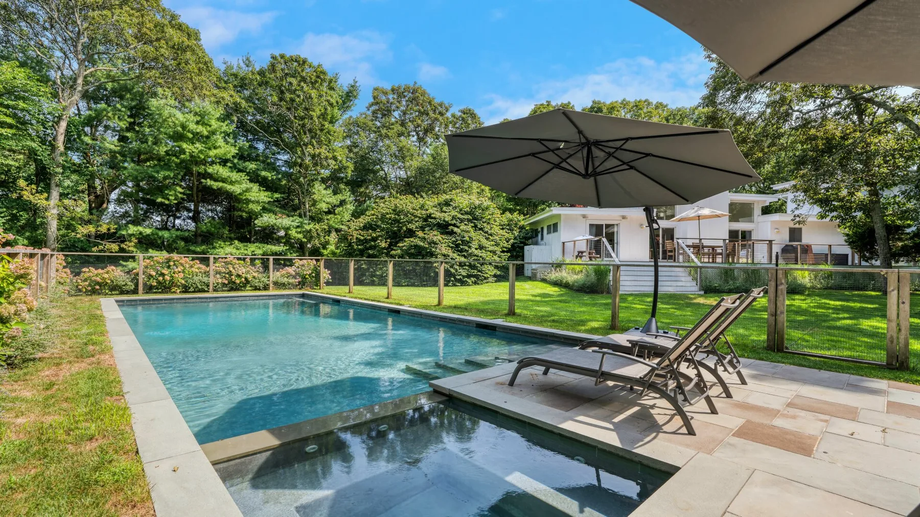 An outdoor pool and adjacent shallow basin sit beside a paved patio with loungers.