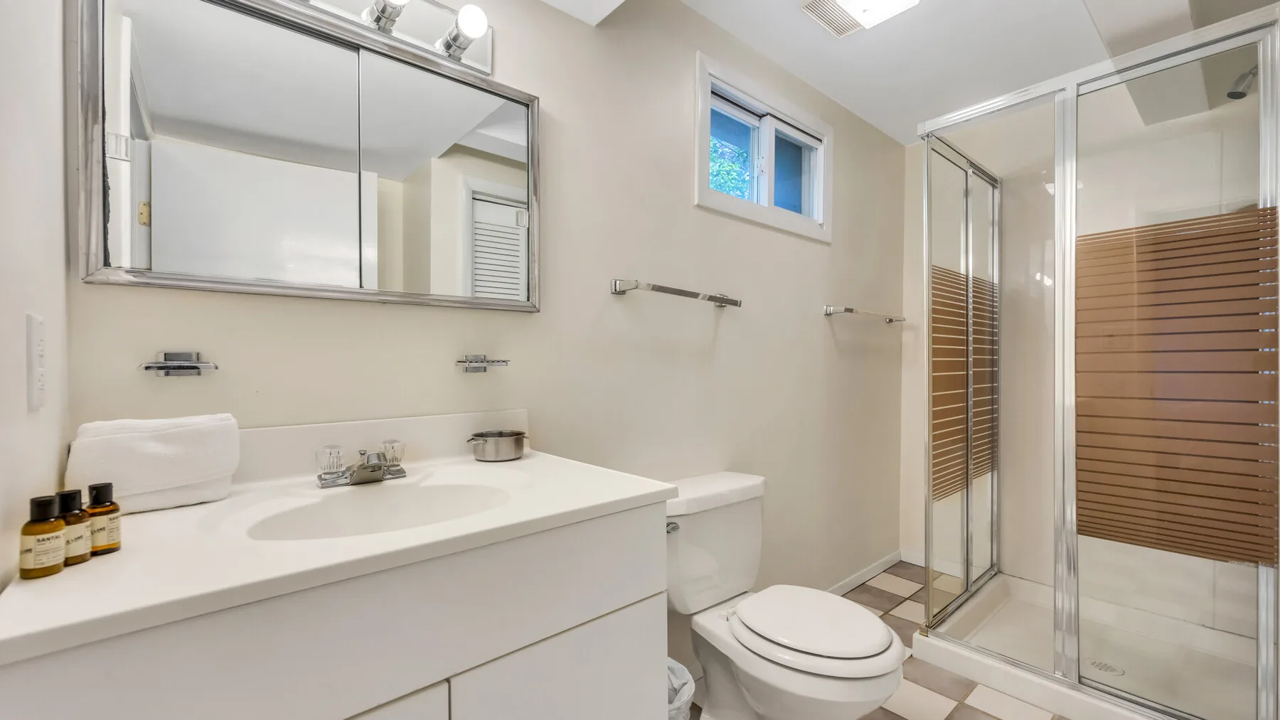A bright bathroom with a wide vanity, mirror, toilet, and glass shower.