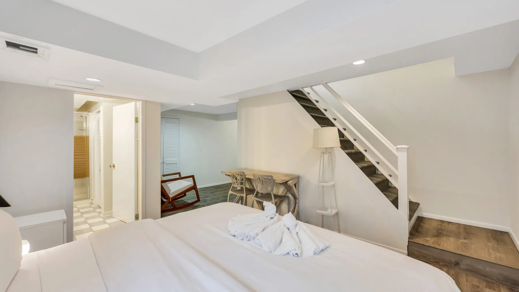 A bedroom with a bed, a small table and chairs, and stairs.