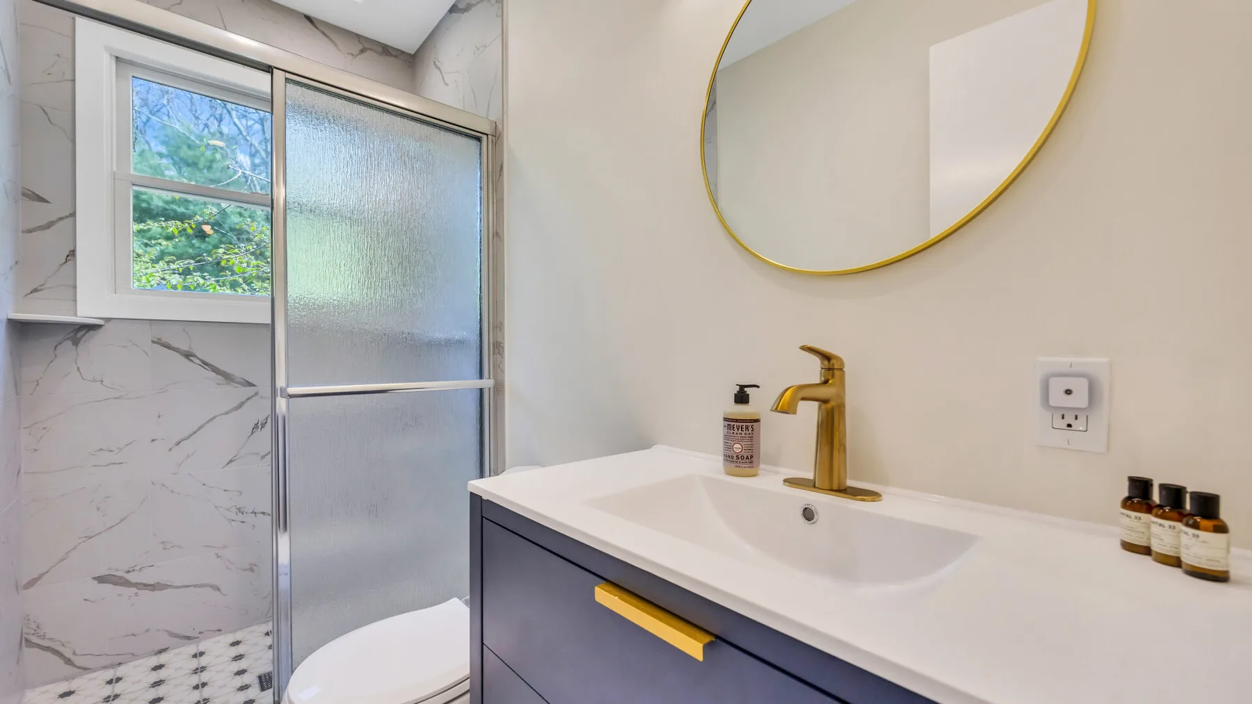 A bathroom vanity with a sink and round mirror beside a shower.