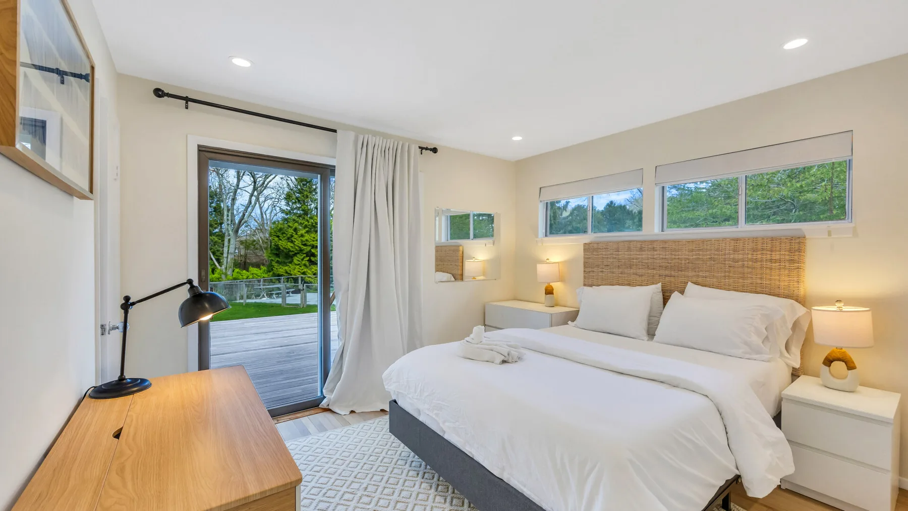A bright bedroom with a neatly made bed and sliding glass doors opening to a deck.