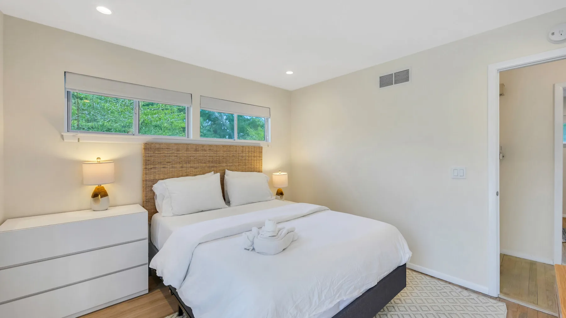 A bright bedroom with a neatly made bed beneath a row of windows.