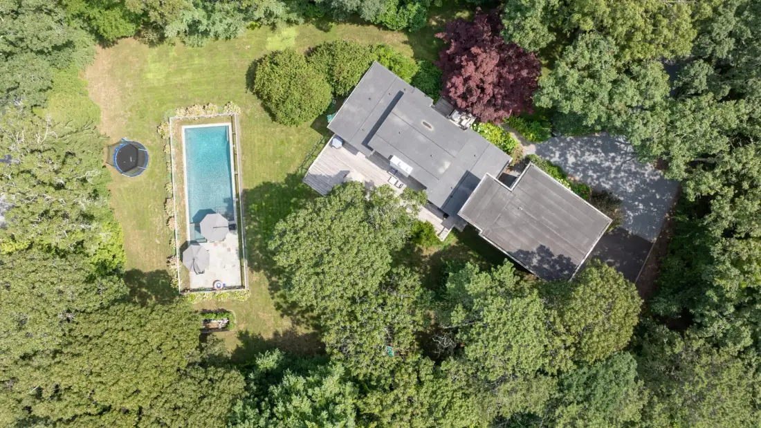 An aerial view shows a house, a swimming pool, and surrounding trees.