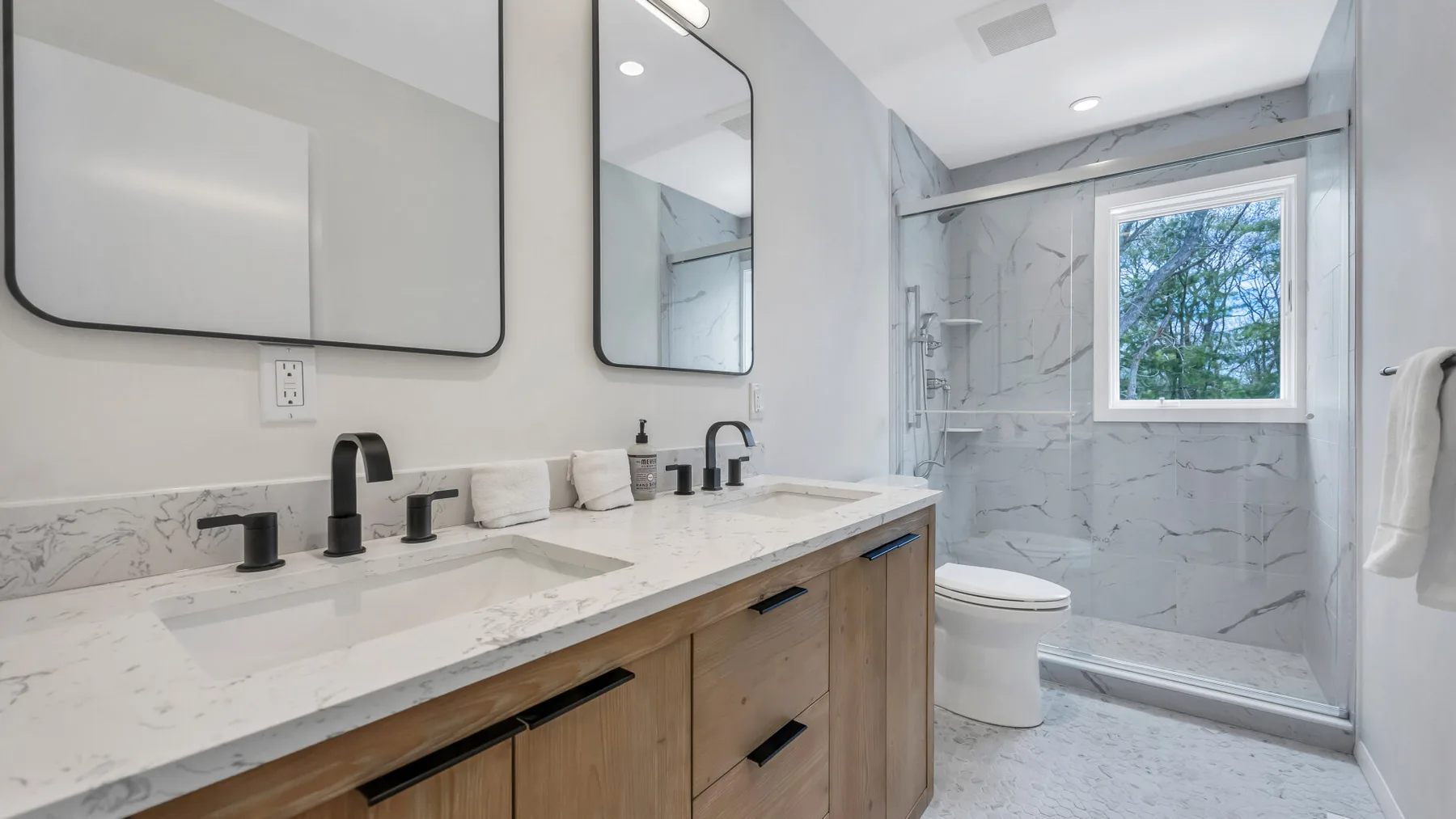 A bright bathroom has a long vanity beside a glass-enclosed shower.