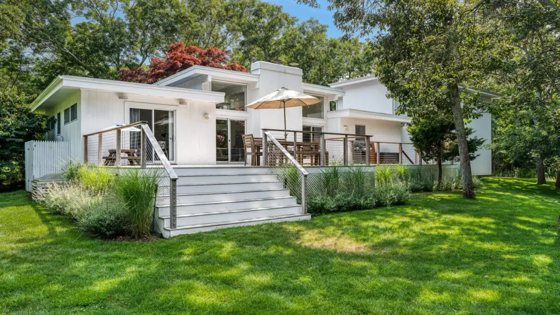 A white house with a raised deck, outdoor seating, and a green lawn.