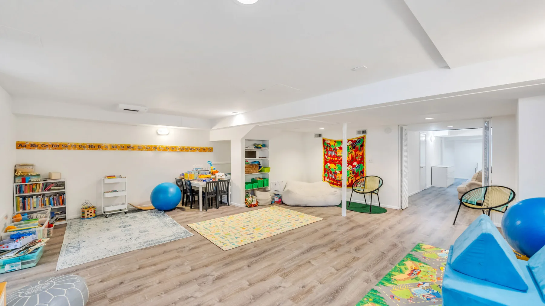 A spacious playroom with colorful rugs, children's furniture, and scattered toys.