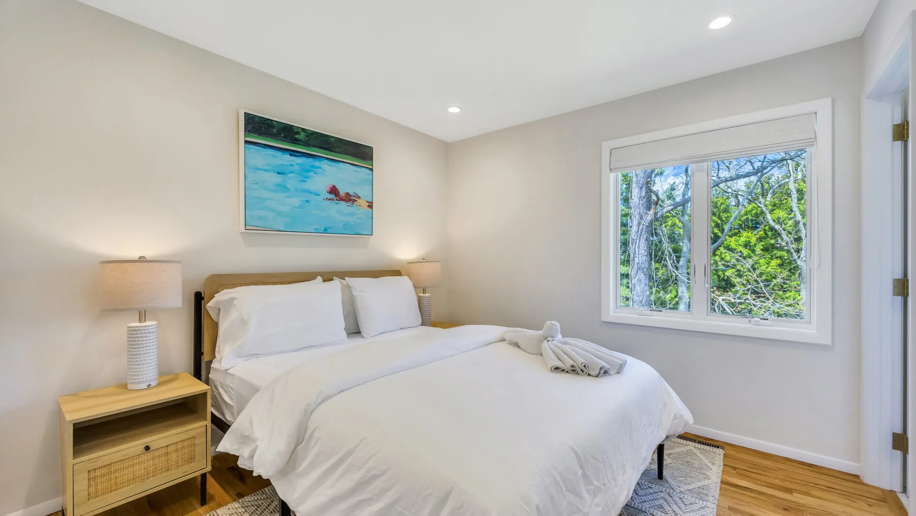 A bright bedroom with a neatly made bed and a large window overlooking trees.