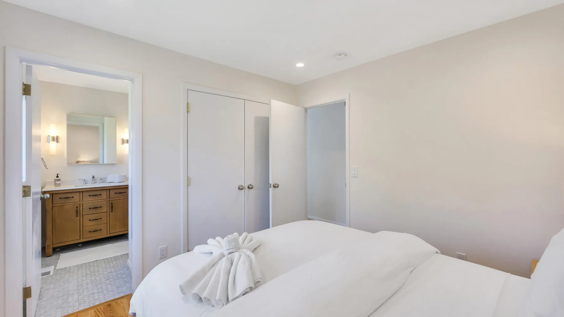 A bedroom with a neatly made bed and an open doorway to the bathroom.