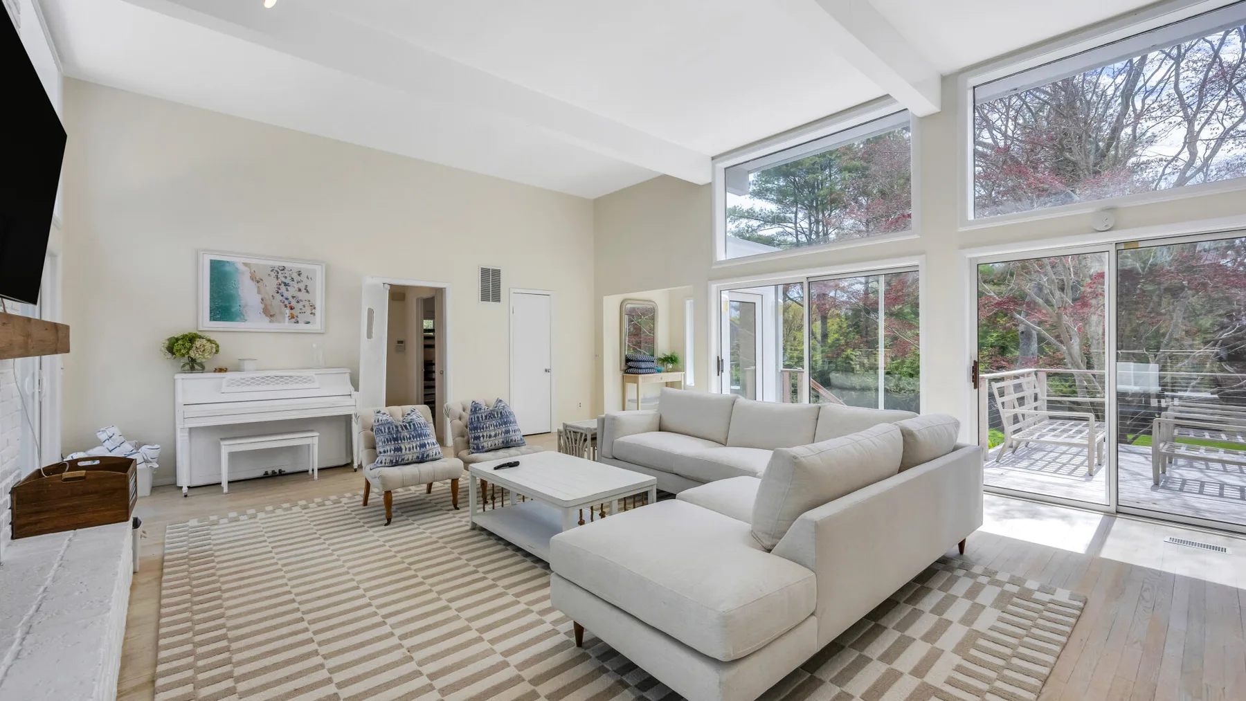 A bright living room with light-colored seating and large windows overlooking greenery.