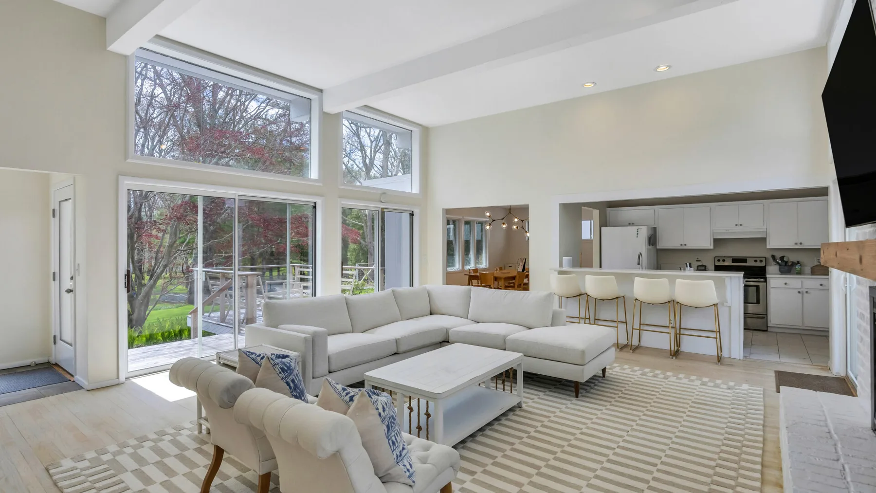 A bright open-plan living room and kitchen with large windows and seating.