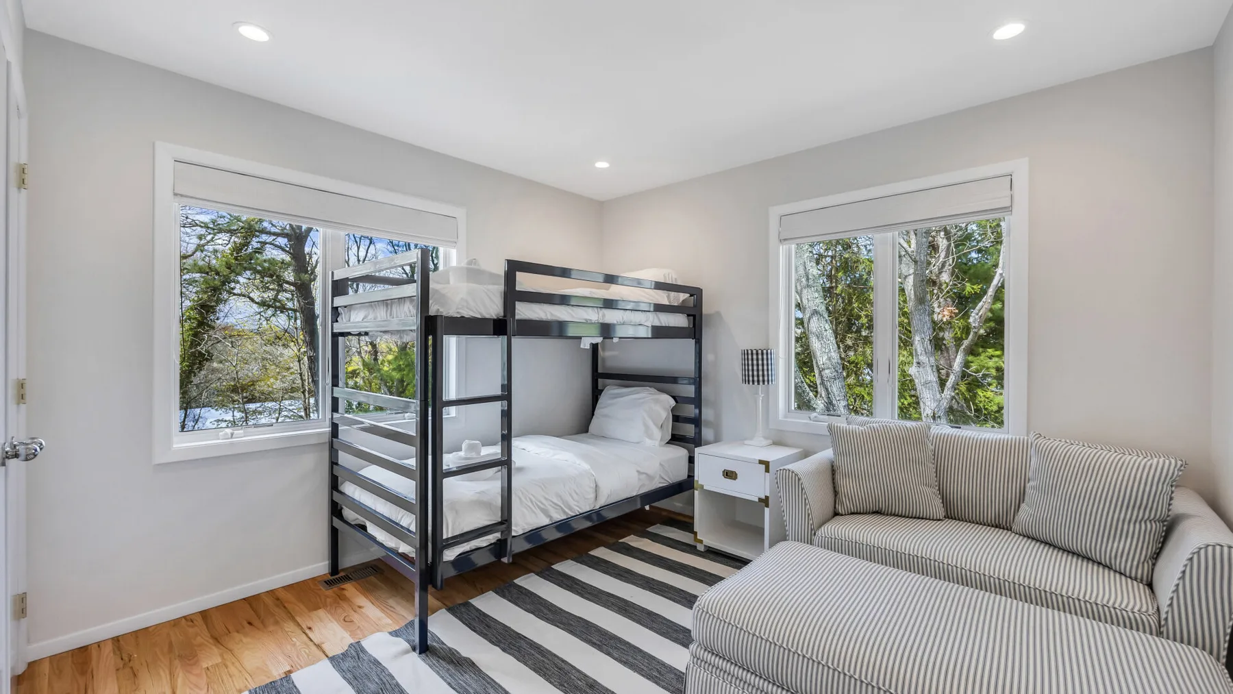 A bright bedroom with a bunk bed and striped seating beside two windows.