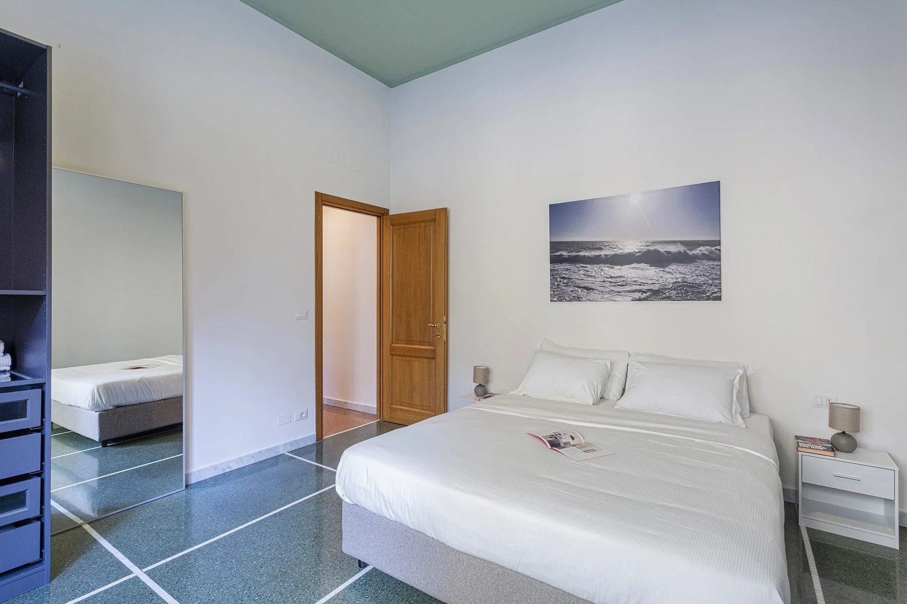 Un dormitorio con una cama bien tendida y una fotografía del océano enmarcada en la pared.