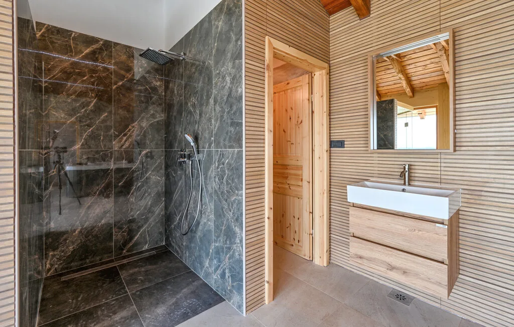Un baño con una ducha revestida de azulejos junto a un tocador de madera y un espejo.
