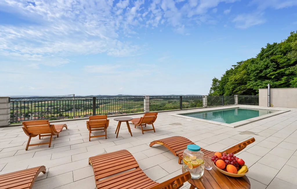 Una terraza exterior embaldosada con asientos, una piscina y vistas al paisaje.