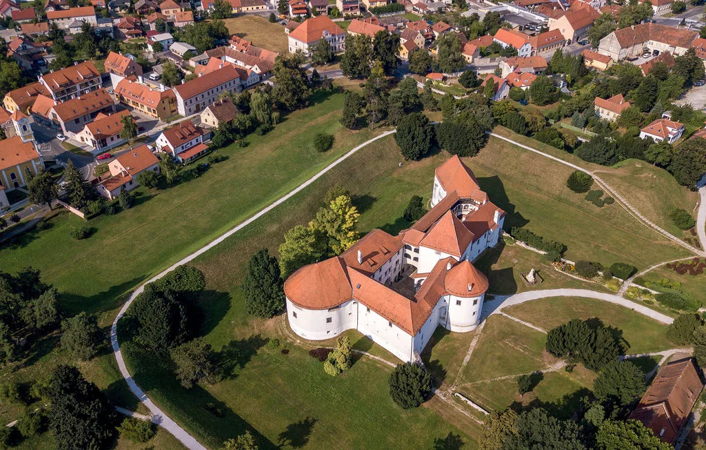 Vista aérea de un castillo histórico con tejados de tejas rojas entre zonas verdes.