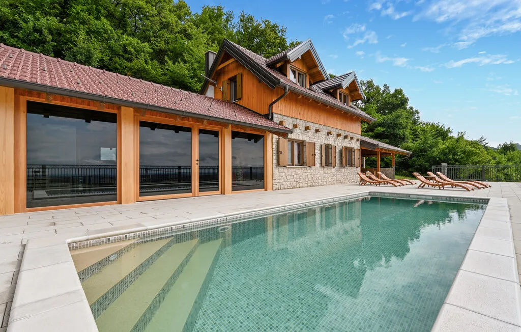 Una piscina junto a una casa grande revestida de madera, con tumbonas junto a la terraza.