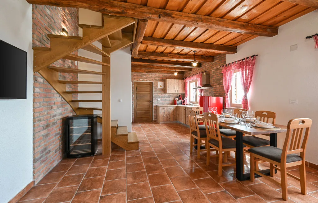 Una zona de comedor y cocina está bajo vigas de madera, con una escalera junto a la pared de ladrillo.