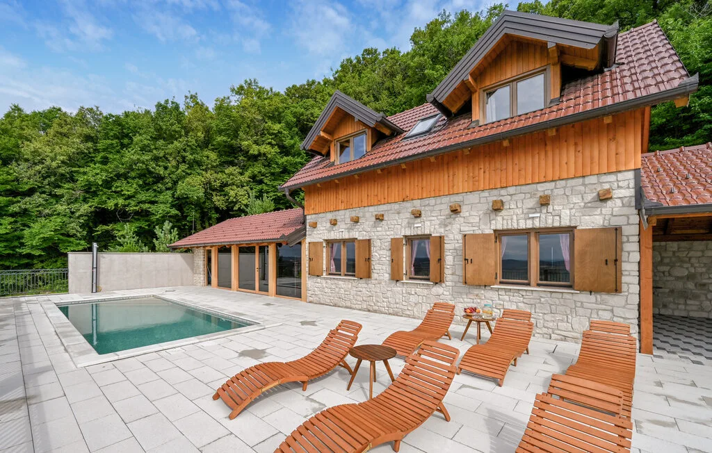 Una casa de piedra y madera da a una terraza pavimentada con piscina y asientos.