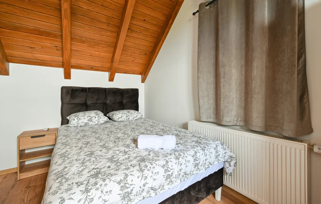 Un dormitorio con una cama doble bajo un techo inclinado de madera y una ventana con cortinas.