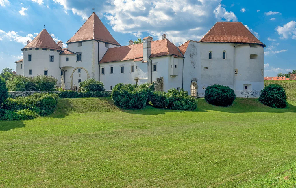 Un edificio blanco parecido a un castillo, con tejados rojos, se alza tras un amplio césped verde.