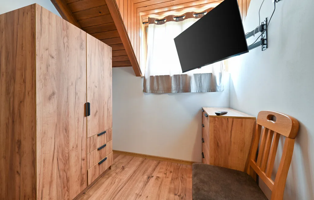 Una habitación amueblada de madera con armario, escritorio, silla y televisor en la pared.
