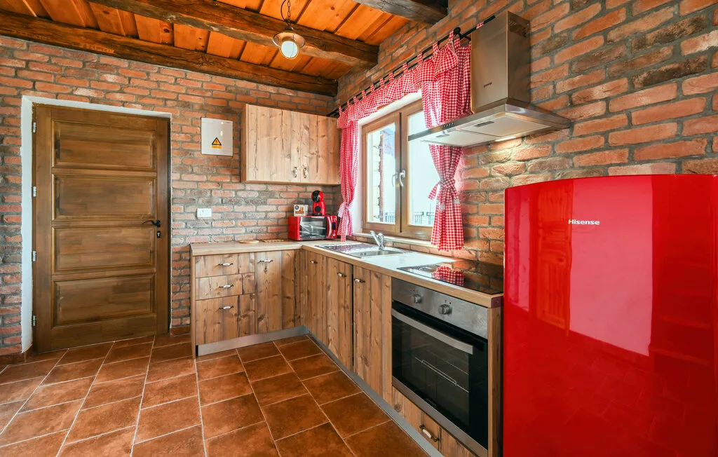 Una cocina rústica con gabinetes de madera, un refrigerador rojo y una ventana.