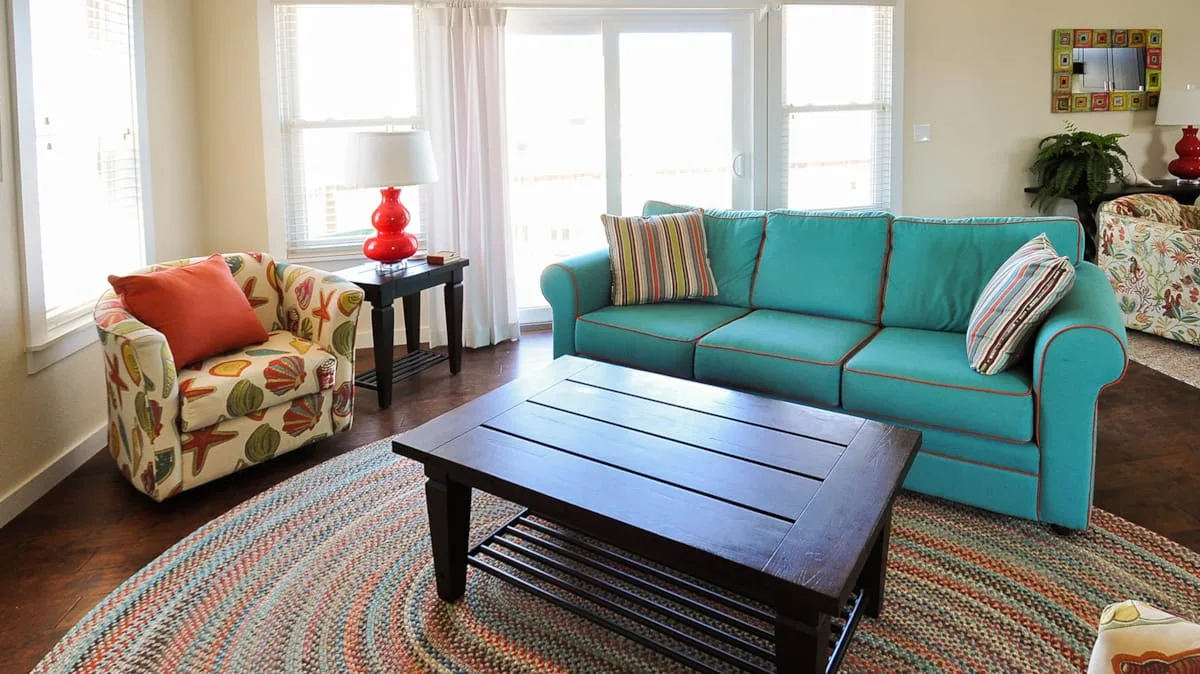 Una sala luminosa con asientos turquesa, un sillón estampado y una mesa de centro oscura.