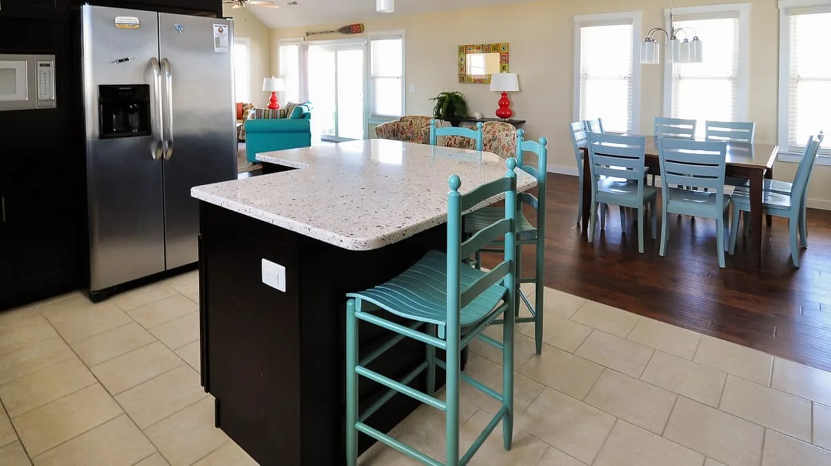 Una cocina y comedor luminosos con una isla grande y asientos color turquesa.