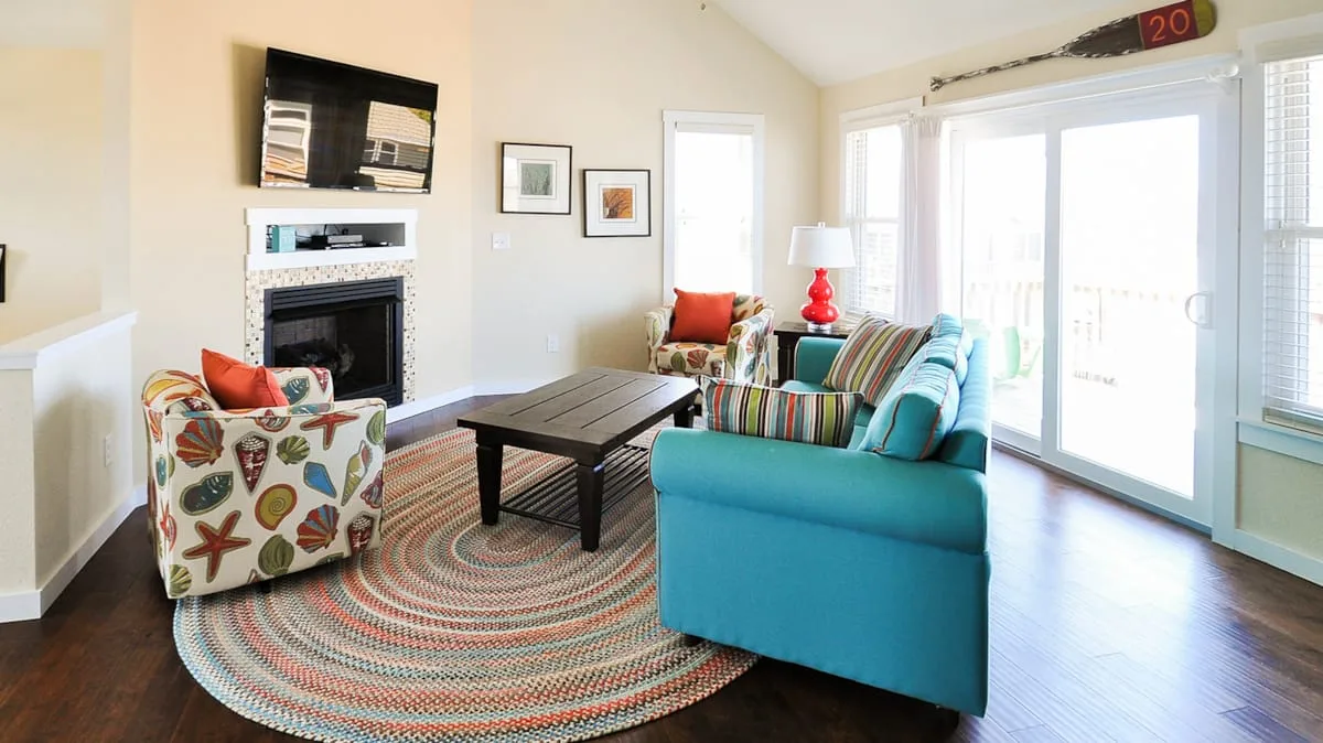 Una sala luminosa tiene asientos coloridos alrededor de una mesa de centro y una chimenea.