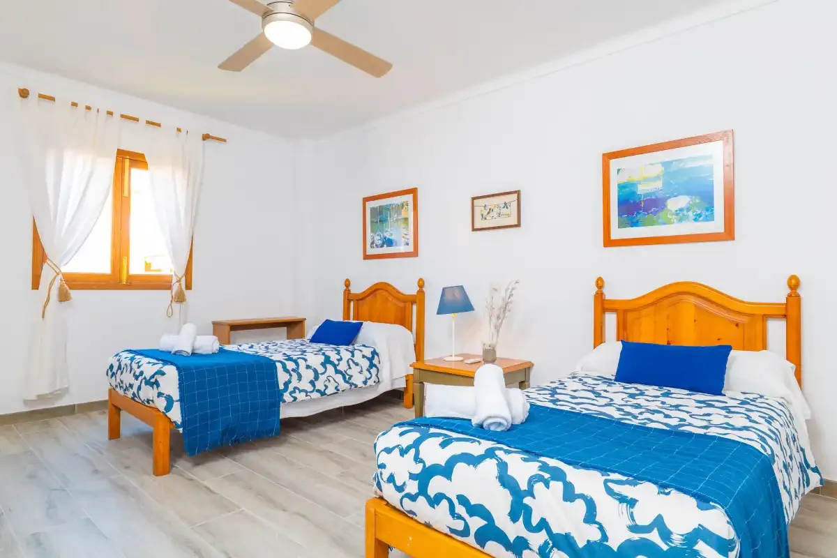 Un dormitorio luminoso con dos camas vestidas con ropa de cama azul y blanca.