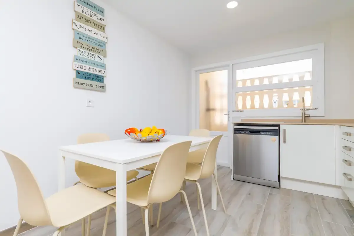 Un comedor luminoso con una mesa blanca y sillas claras junto a la cocina.
