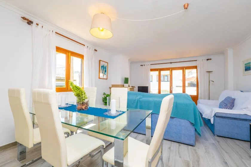 Una luminosa sala de estar y comedor tiene una mesa de vidrio, asientos y muebles cubiertos de azul.